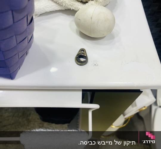 חפץ מתכת קטן על משטח לבן ליד מגבת